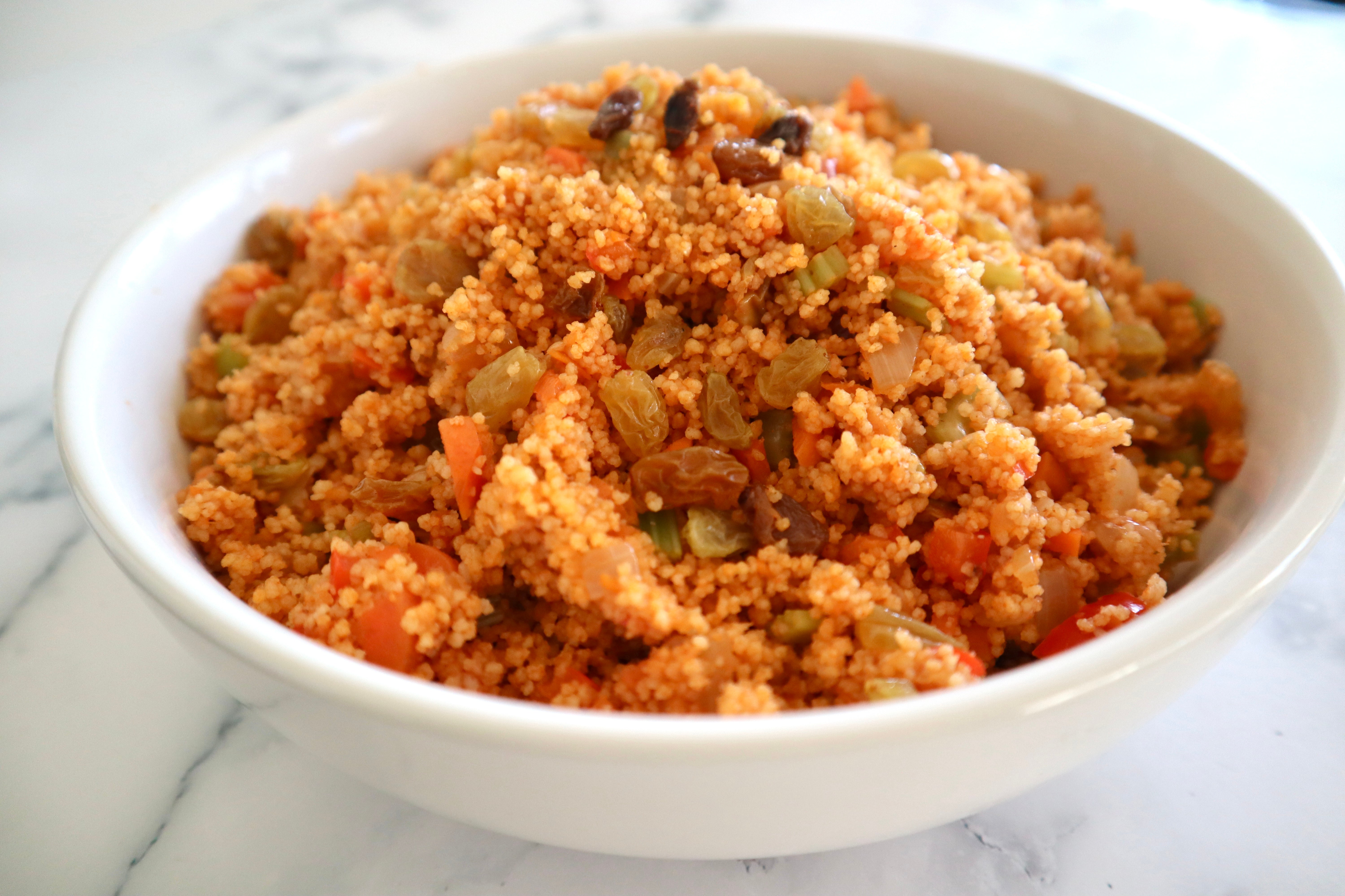 White bowl filled with harissa spiced couscous and golden raisins. 