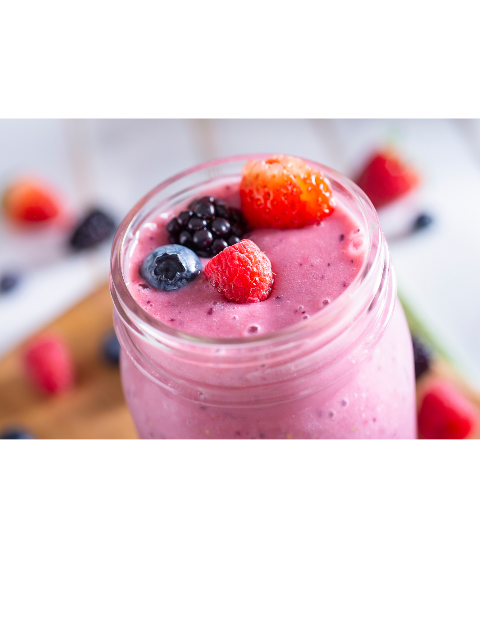 Pink berry smoothie in a glass cup, with mixed berries on top. 