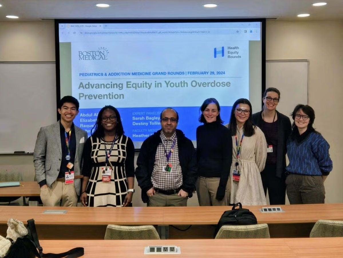 Group photo: seven individuals standing in front of a projector screen that displays the words 'Advancing Equity in Youth Overdose Prevention'