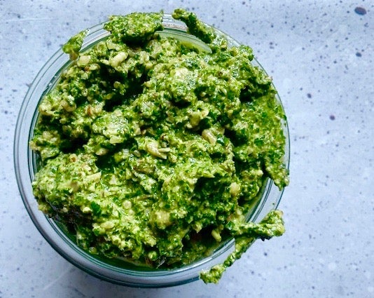 A jar overfilled with bright green, chunky, basil and walnut pesto