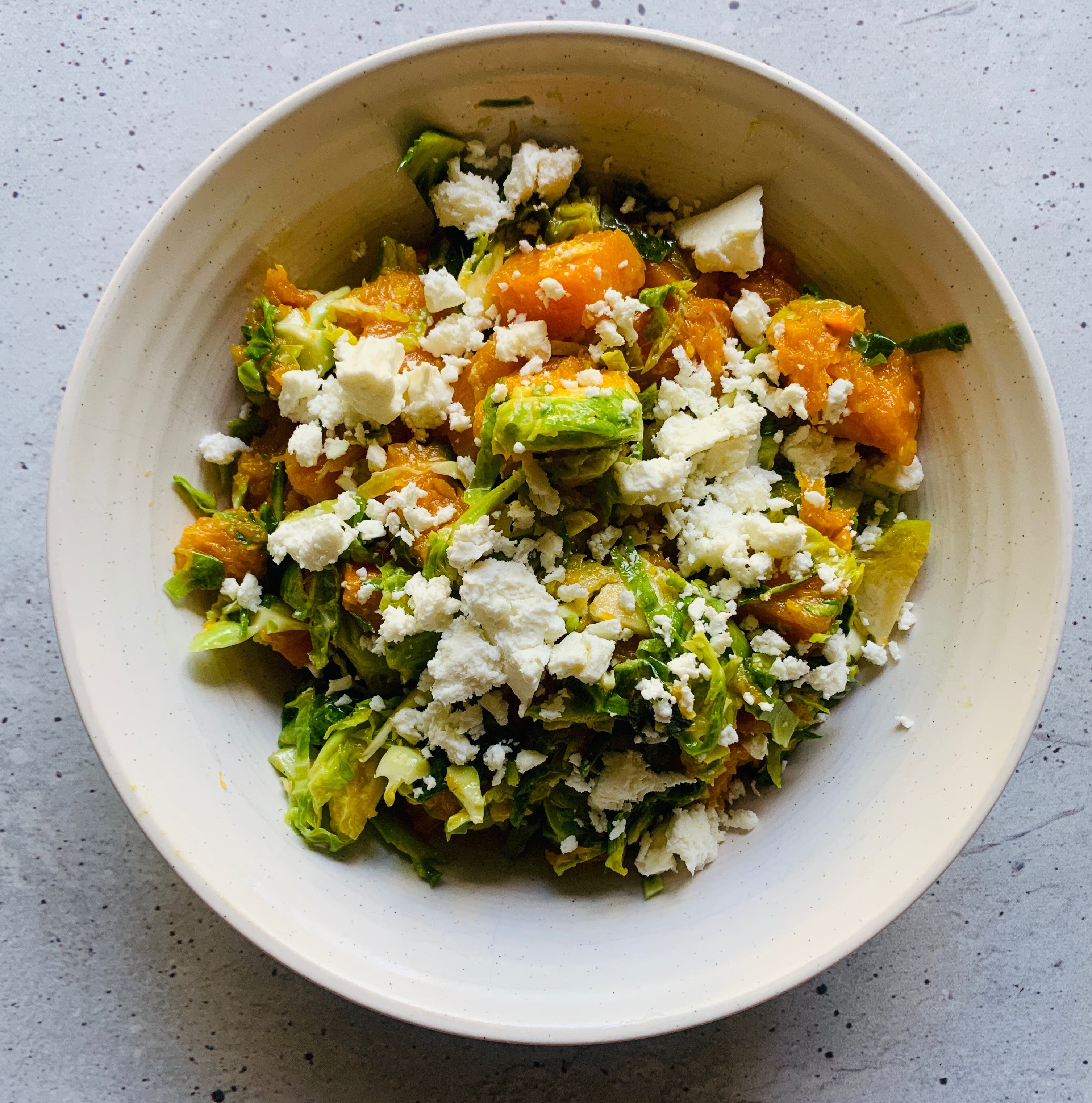 Photo of Butternut Squash and Brussels sprout salad in a white bowl, sprinkled with feta cheese.