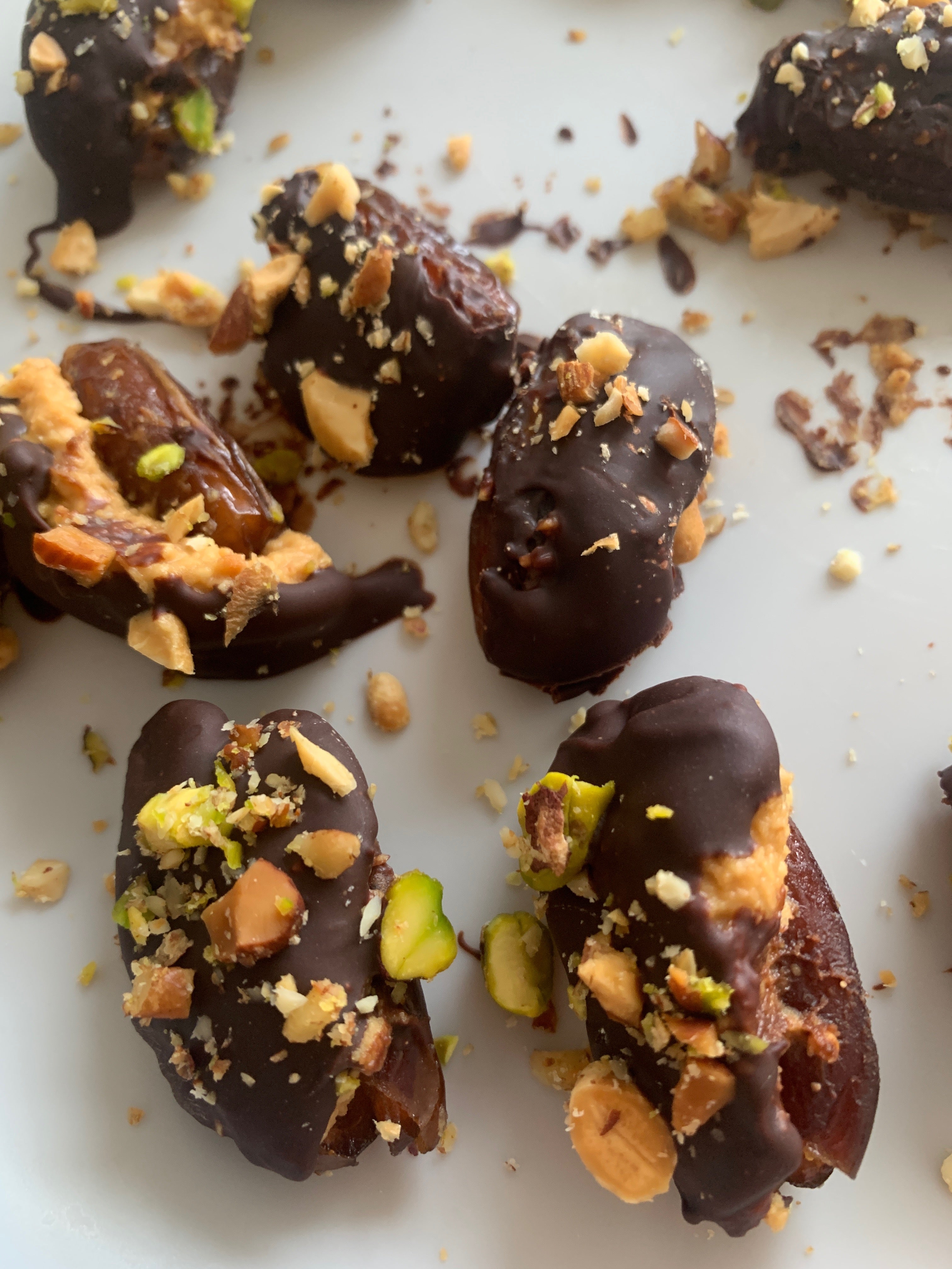 Dátiles, cubiertos de chocolate, con frutos secos triturados espolvoreados por encima. En un plato blanco.