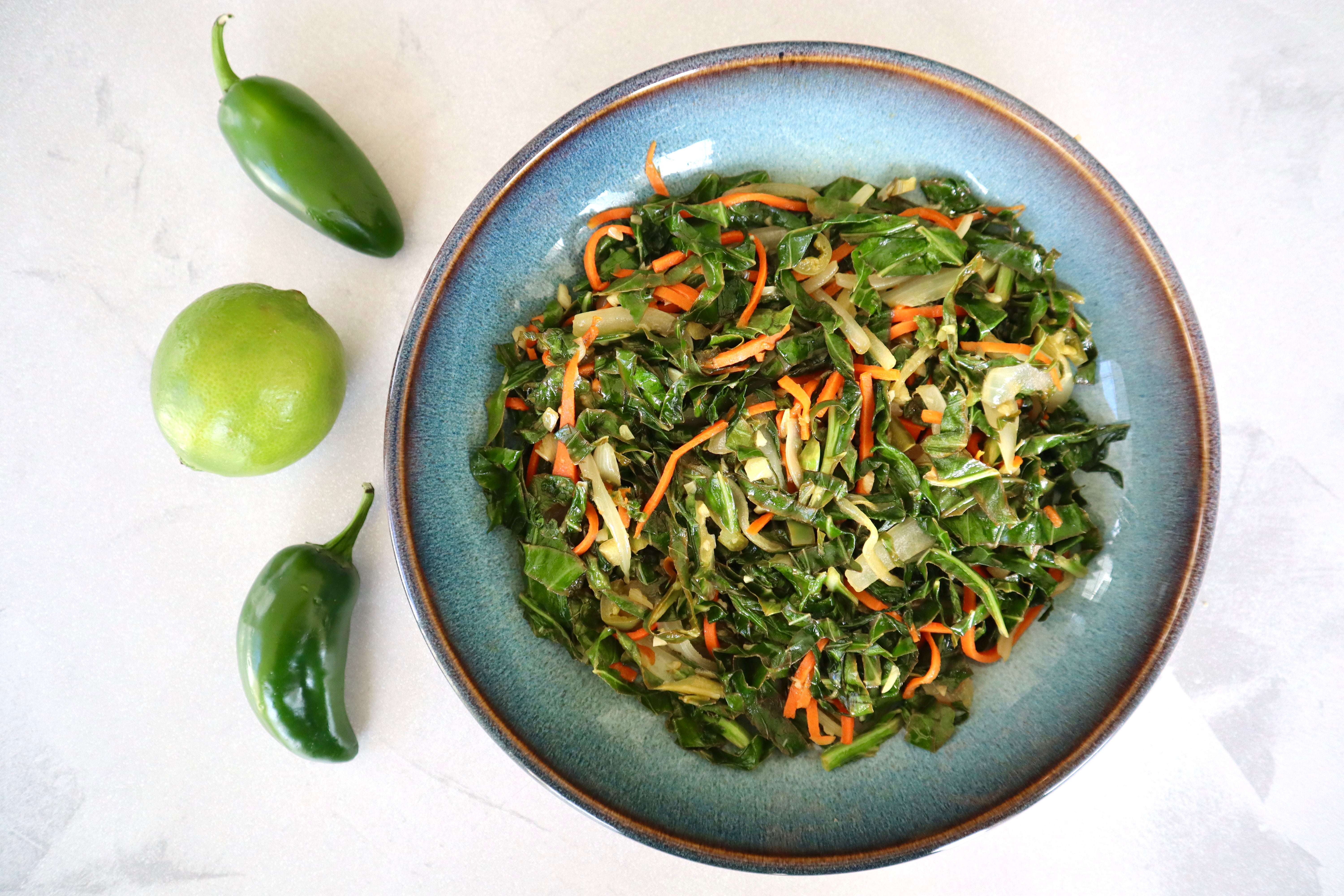Blue bowl filled with ribbons of collard greens and carrots. A lime and two jalapeños are on the side of the bowl. 