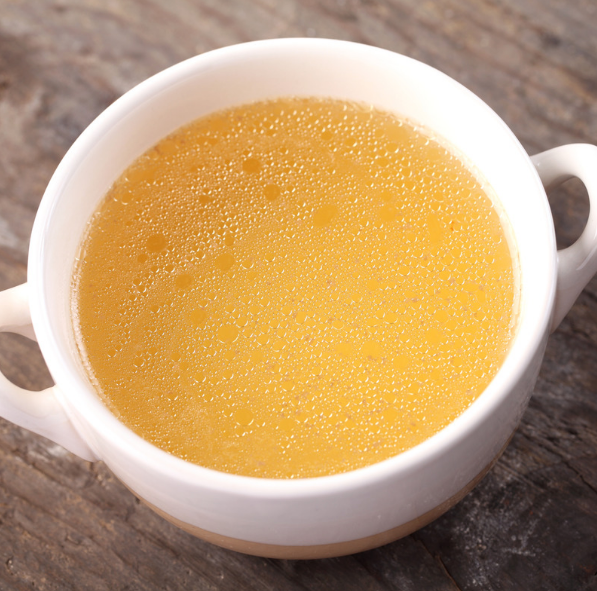 A white bowl with handles on either side, filled with a golden broth.