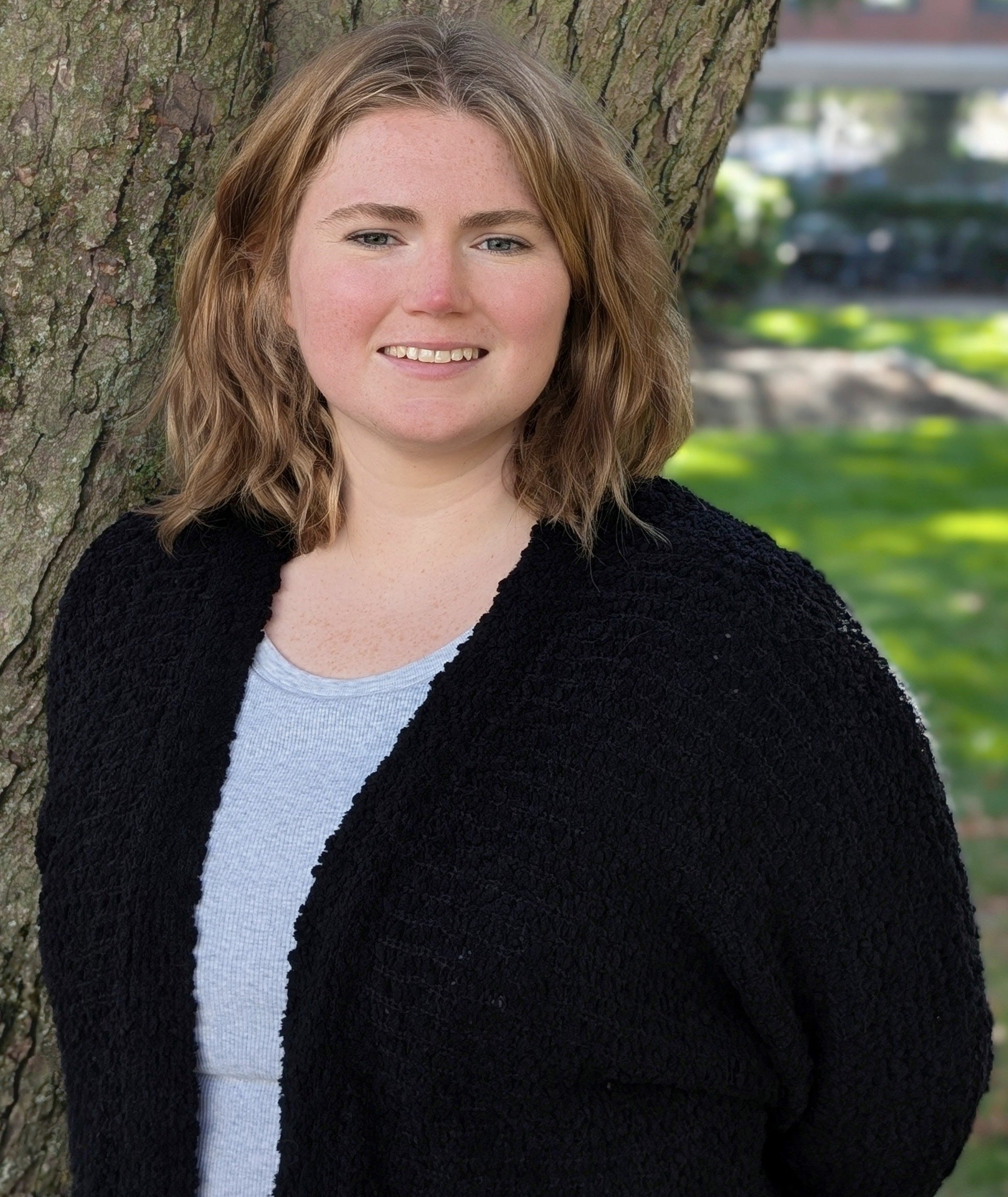 woman in black jacket and blue shirt in front of a tree
