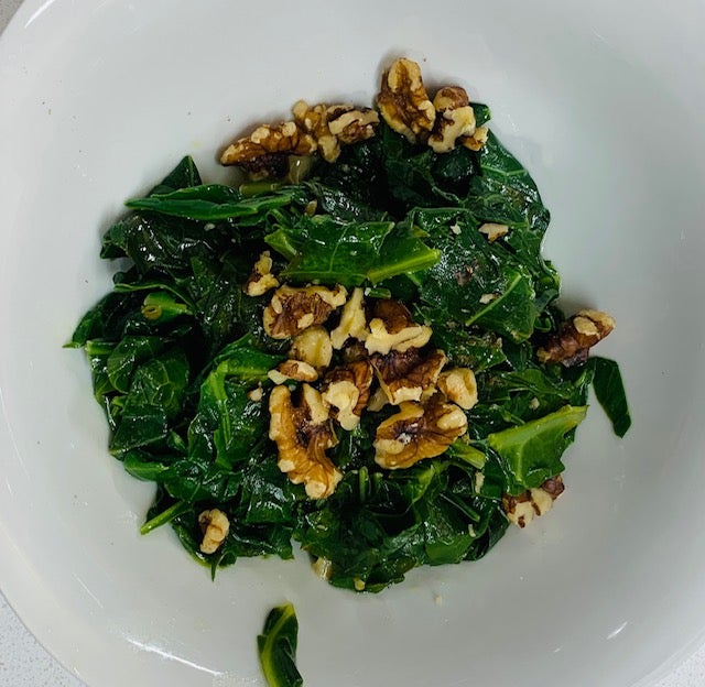 sauteed collards with walnuts on top, in a white bowl