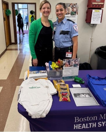 picture of two women behind a table with onesies and snacks