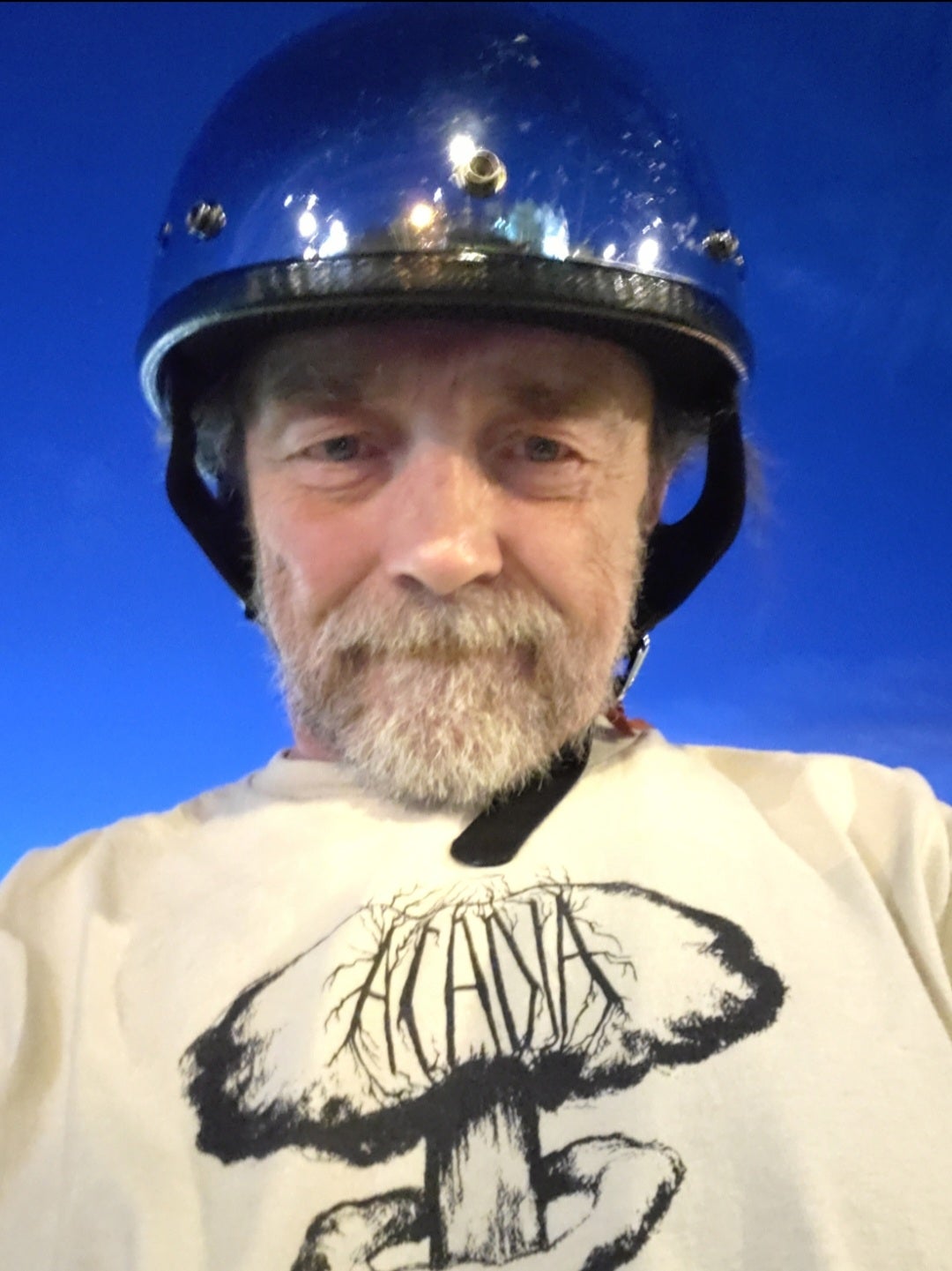 Headshot of Peter Goudy, a white man with a beard wearing a blue motorcycle helmet and a T-shirt of his own design