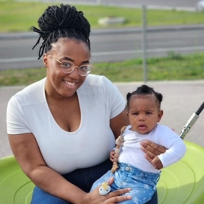 Kibriyaa sitting on a playground swing and holding her infant daughter, Adaira