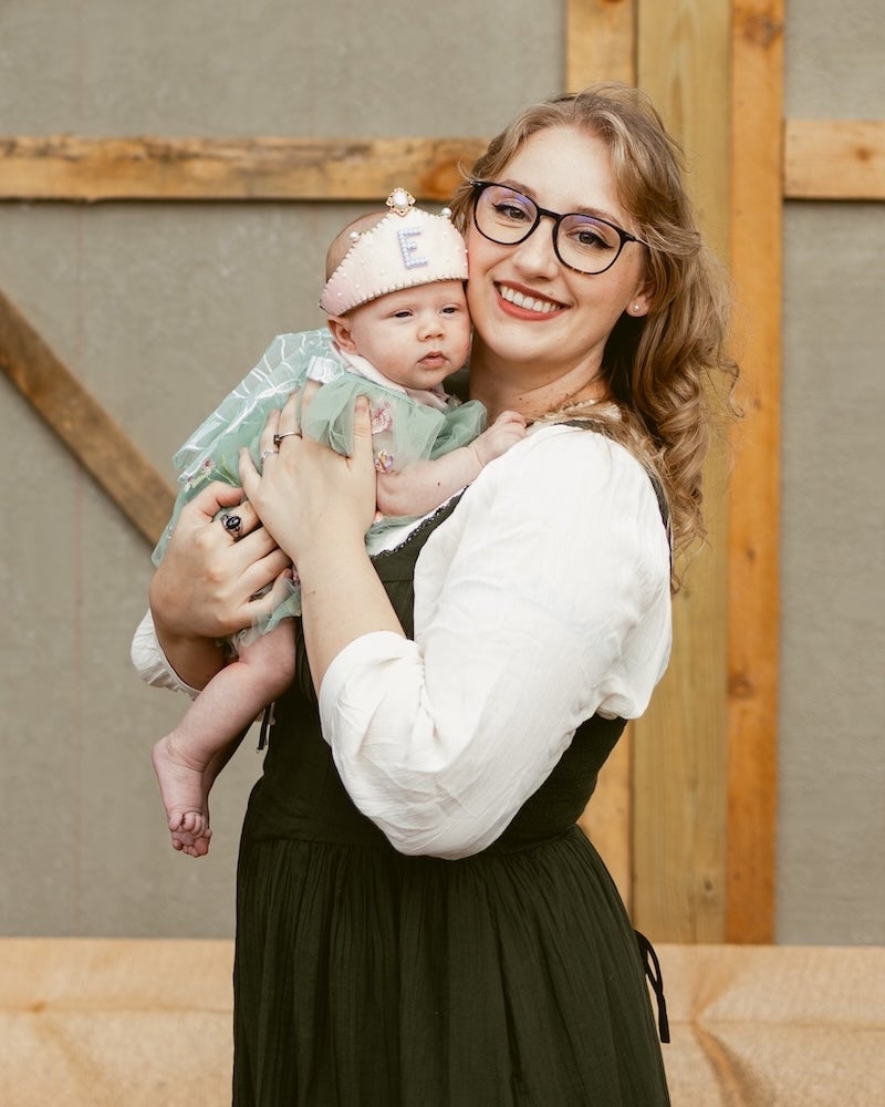 Mom Lauren Skelton grinning while holding a sleepy-looking baby Elora, both of them dressed in Renaissance costumes