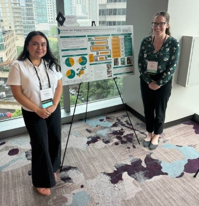 two women with research poster in front of window