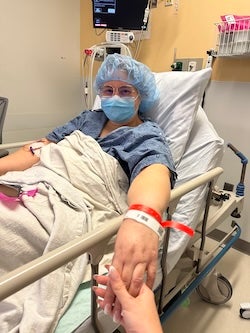 BMC patient Katia Santos, masked and prepped for thoracic surgery, reaches a hand towards the viewer, where another hand is seen grasping hers