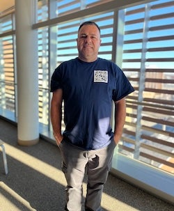 Luis Mendes stands tall in front of a window with a view of downtown Boston