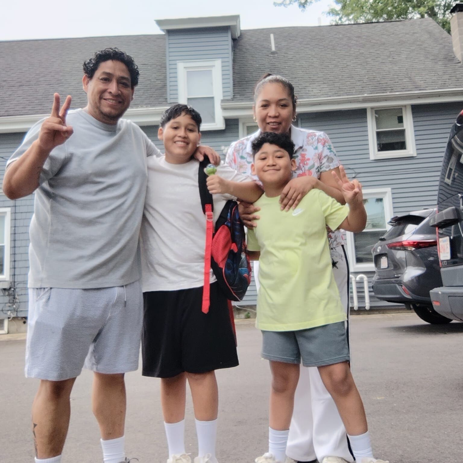 BMC pediatric surgery patient Dylan makes a peace sign while standing with his father, mother, and older brother