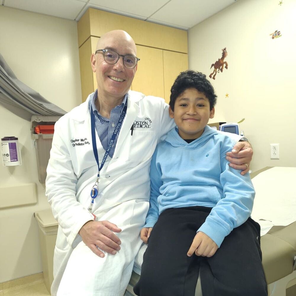 BMC patient Dylan sits smiling next to his surgeon, Dr. Christopher Muratore