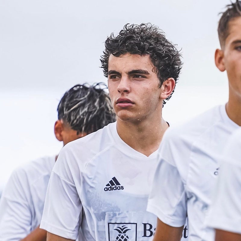 A young adult, sweating from exertion, stands with a group of fellow players and stares glumly into the middle distance