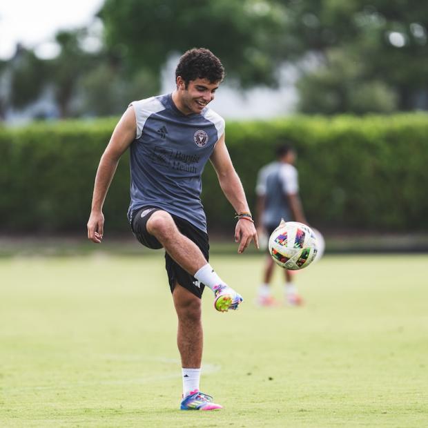 A young man grins to himself as he practices dribbling a soccer ball on a sunny field