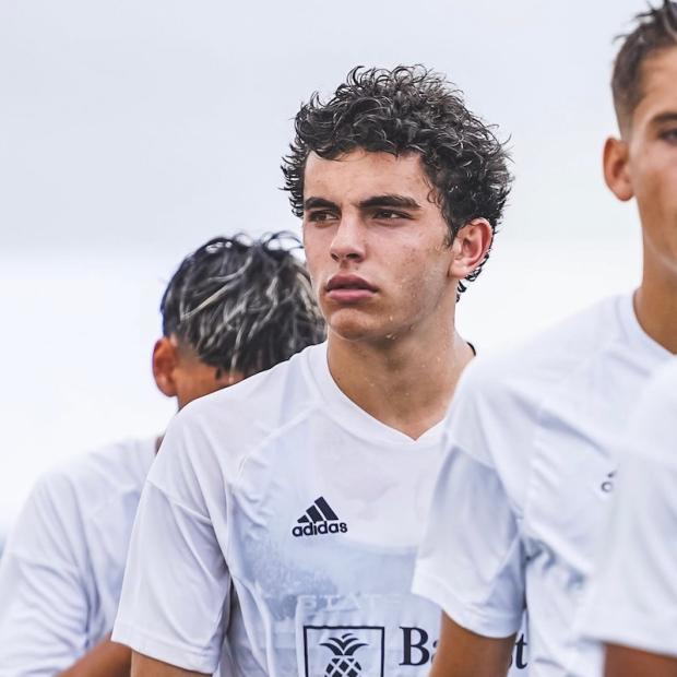 A young adult, sweating from exertion, stands with a group of fellow players and stares glumly into the middle distance