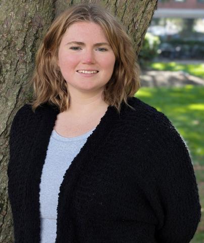 woman in black jacket and blue shirt in front of a tree